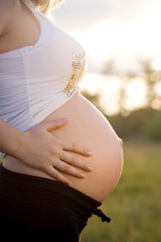 pregnant woman staying on meadow and holding belly