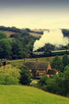 A steam train emerging from Corfe Castle railway station in Dorset UK. A tilt and retro effect has been applied to the image.