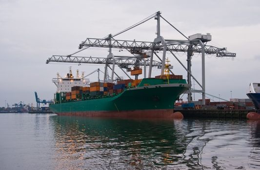 Containership with cranes in harbour on cloudy evening