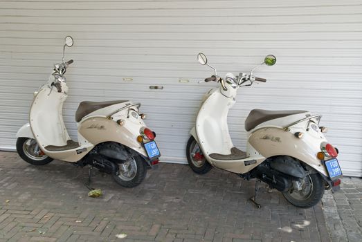 Two scooters parked on pavement, beside a building in the Netherlands. 