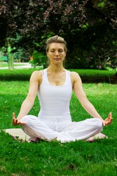 Blonde girl in nature green park exercising yoga, fitness program