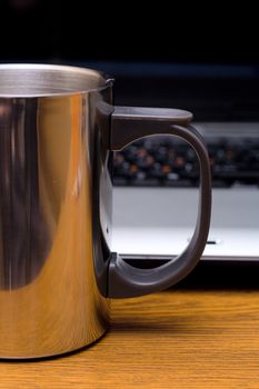 metal cup before laptop, on wooden table
