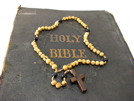 A rosary laying on a worn antique Bible.