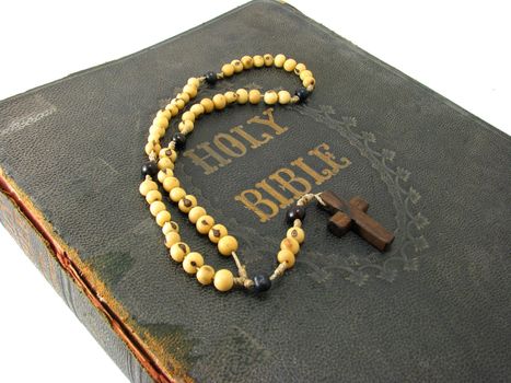 A rosary laying on a worn antique Bible.