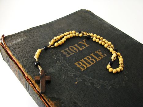 A rosary laying on a worn antique Bible.