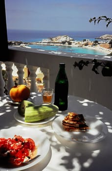 Detail of a dinner table on a balcony with bay and beach in the background