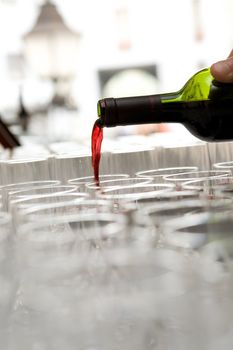 Red French wine pour from a bottle in the glasses which are standing in a row
