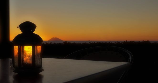 Lamp on table overlooking Sicilian Volcano island at sunset