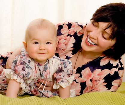 The smiling girl in dress with laughing mum on bed
