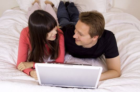 Couple in the 30's using a laptop while laying on the bed