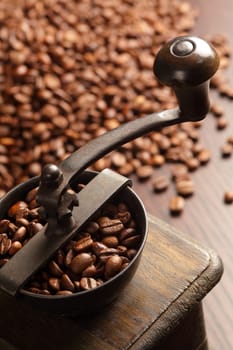 Photo of an antique coffee grinder with coffee beans in the blurred background.
