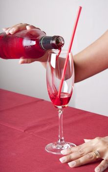 Red cocktail in a glass with a straw and a bottle. The content of the bottle is poured into the glass.