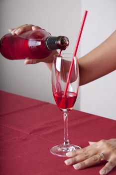 Red cocktail in a glass with a straw and a bottle. The content of the bottle is poured into the glass.