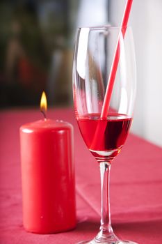 Red cocktail in a glass with a straw and a red candle