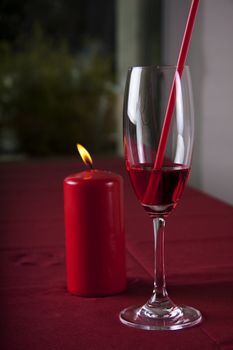 Red cocktail in a glass with a straw and a red candle in the background