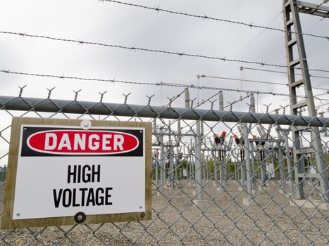 High-voltage transformer substation behind barbed-wire chain-link fence with Danger High Voltage sign.