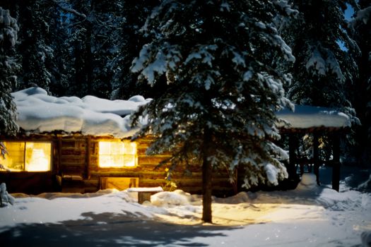 Yukon/Alaska trapline log-cabin fully illuminated at full-moon night in snowy winter.