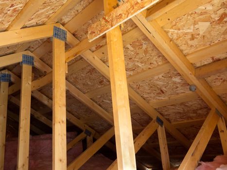 Attic formed by trusses, OSB boards and fiberglass insulation under the roof of residential house.