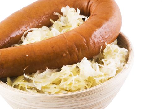 Close up of a wooden bowl with sauerkraut and a smoked sausage.