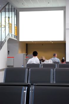 People Waiting in Airport Hall in front of Blank Billboard