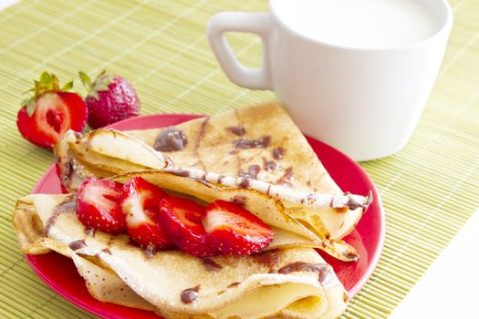 sweet pancakes with strawberry and cup of milk on white background