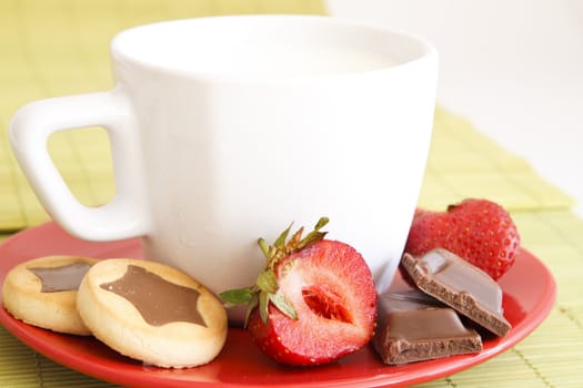 sweet meal with cup of milk and cakes and chocholate and strawberries