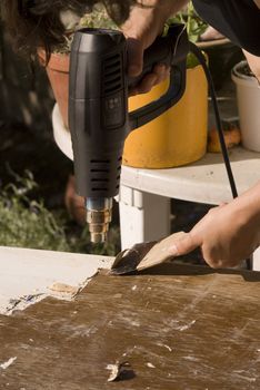 portrait of renovation; removing old paint using scraper and heat gun