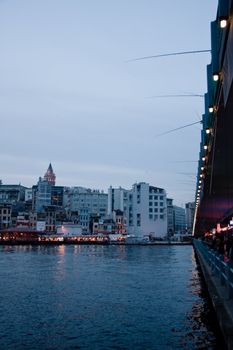 Galata tower illuminated in the evening by bridge with fishermen on parapet of bridge