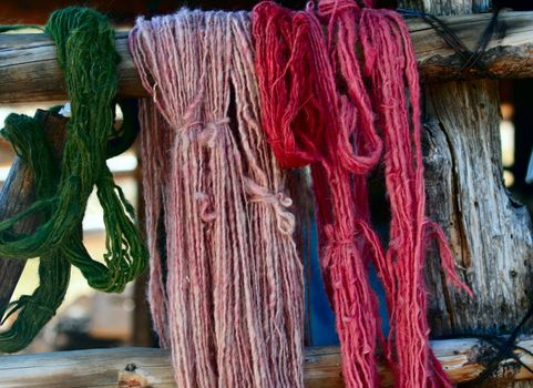 Skeins of various shades of natural dyed handspun yarn hang on a corral fence pole to dry in the New Mexico sunshine.  
