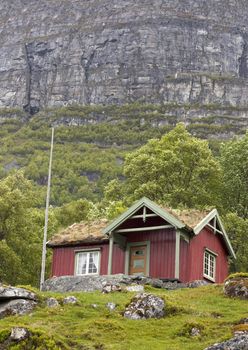 Red cabin with turf roof against a steep mountain cliff