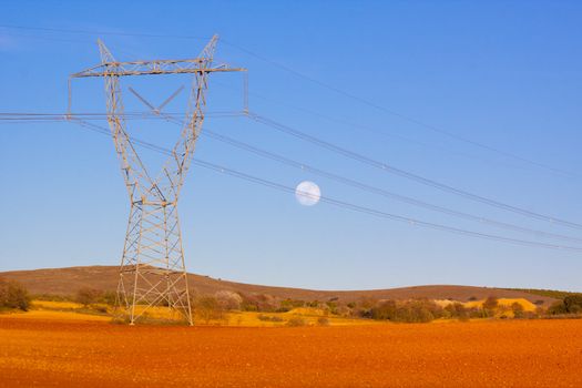 High tension 
transmission lines crossing the colorful fields with moon in the sky.