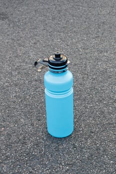 A blue water bottle on asphalt