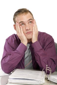 Exhausted man in the office with files on. He keeps his hands to his face and sad looks up 