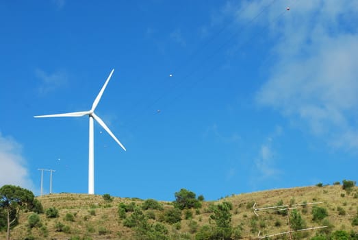 photo of a wind turbine with sky background on a green mountain