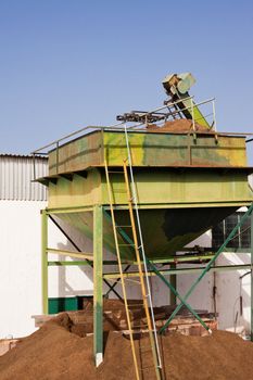 Exhausted olive pulp (orujo) from busy olive oil mill factory being conveyed into huge metal silo container for later composting.