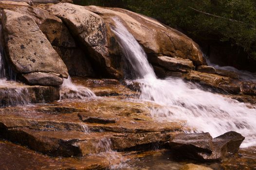 Small single waterfall cascading down mountain boulders into shallow water