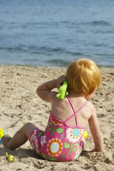 Little baby with a phone in her hand, on the beach