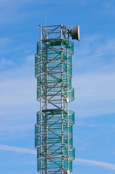 Telecommunications mast set against blue sky and small clouds