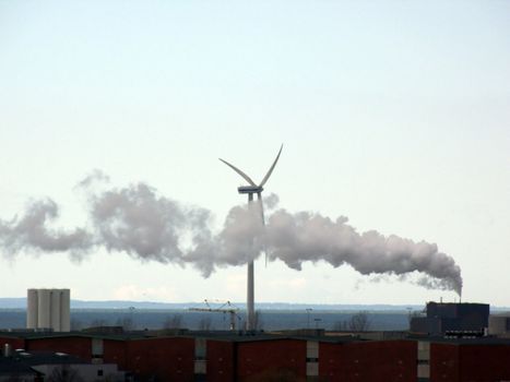 portrait of industry smoke passing wind turbine