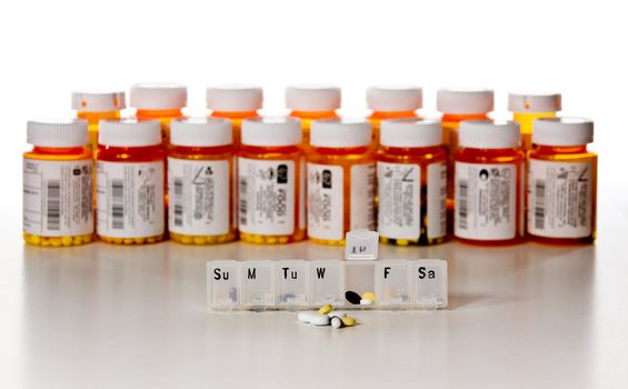 Row of drug bottles with a weekly pill holder open in front and in focus