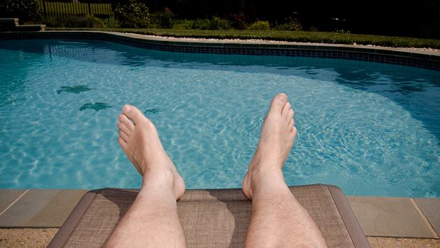Middle-aged man's feet overhanging blue swimming pool
