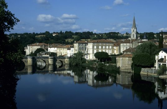 Old french town reflected in a still river crossed by a stone arched bridge