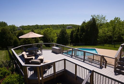 Modern wooden deck with seats and umbrella overlooking a blue pool