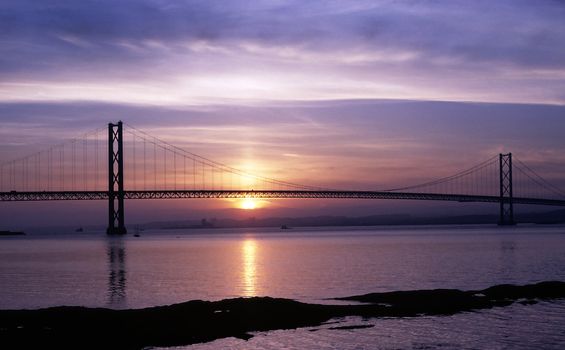 Forth Road Bridge near Edinburgh at sunset with the sun reflected in the River Forth