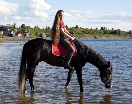 The girl lead a horse to water. Summer landscape.