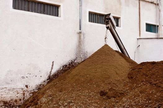 Exhausted olive pulp (Orujo), ready to compost, piles up in the back of busy olive oil mill factory.