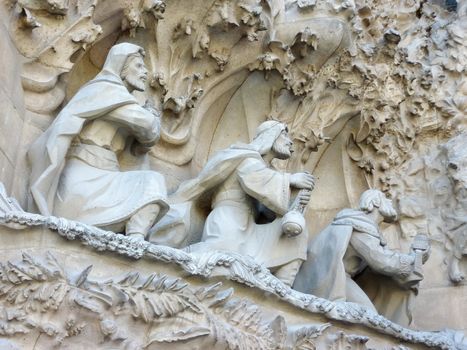 Close up of three men praying sculptures on the Sagrada familia cathedral, Barcelona, Spain. The building of this cathedral strated in 1882 by famous architect Antoni Gaudi and is not finished yet. Its style is neogothic. In 2005, Unesco entered this cathedral in worl heritage.