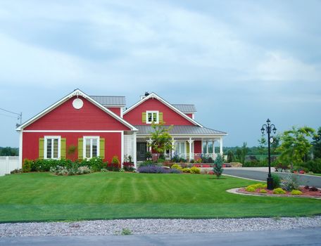 Red houses and beautiful garden with green grass along road 138 in Quebec, Canada, by cloudy weather