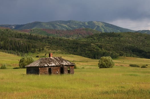 An old building stands in a valley with the Rocky Mountains in the distance.