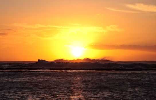 Sun setting on the horizon over strong breaking waves off the coast